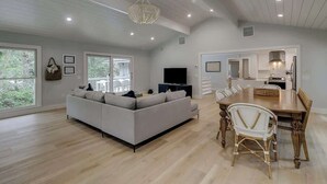A spacious living area with a sofa, dining table, and chairs, a television, and a chandelier.
