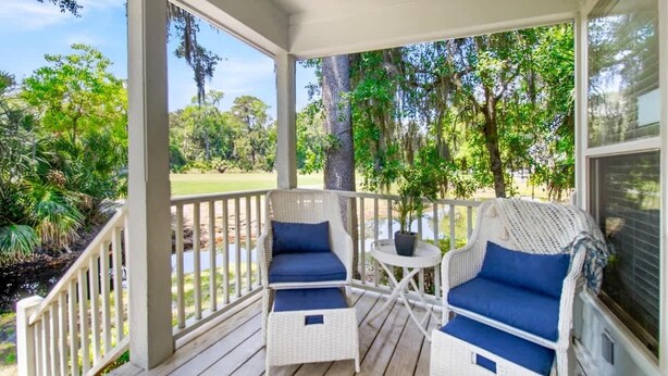 A covered porch with wicker furniture and a view of a green landscape.