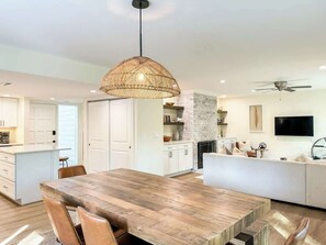 Une cuisine moderne avec une table à manger en bois, des meubles de rangement blancs et un luminaire suspendu.