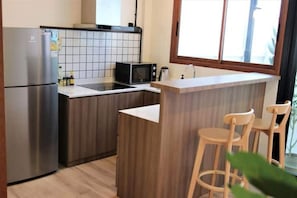 A modern kitchen with a built-in microwave, a stainless steel refrigerator, and a wooden island with bar stools. - Private Cozy Townhouse Near "Lanmuang Village" (Chiangrai)