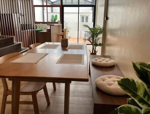 A modern dining area with a wooden table and chairs, a bench with a cushioned seat, and potted plants. - Private Cozy Townhouse Near "Lanmuang Village" (Chiangrai)