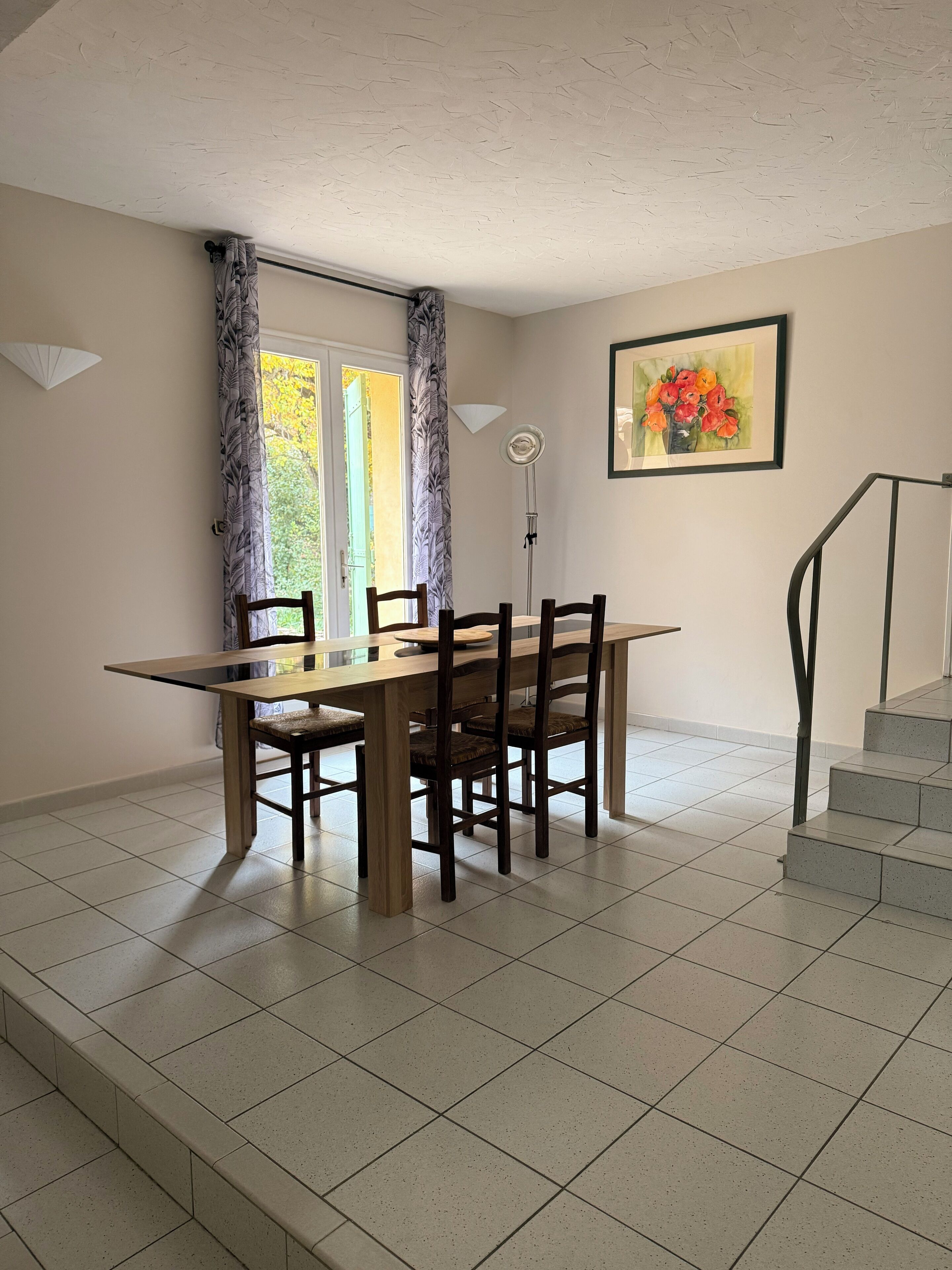 Un coin repas avec une table et des chaises en bois, un tableau accroché au mur et un escalier menant à l’étage.