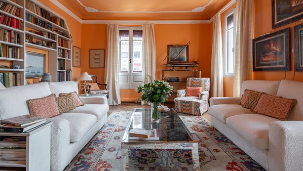 Un salon avec deux canapés blancs, une table basse, une bibliothèque et une grande fenêtre avec des rideaux.