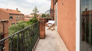 Un balcon avec une chaise et une table, donnant sur un jardin et les bâtiments voisins.