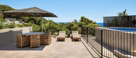 A rooftop terrace with a pool, lounge chairs, and a table with chairs.