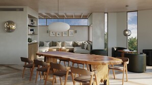 A modern living room with a large wooden dining table, comfortable seating, and a large window offering a view of the outdoors.