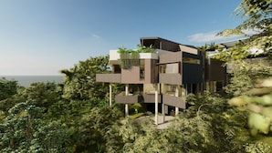 A modern multi-story building with balconies, surrounded by dense greenery and overlooking a body of water.