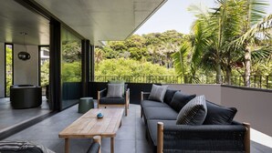 A modern outdoor seating area with a sofa, chairs, and a table, overlooking a lush garden and trees.