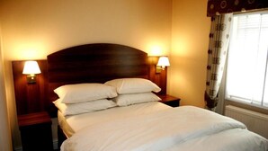 A hotel room with a large bed, two bedside lamps, and a window with curtains. - The Railway Tavern Hotel (London)