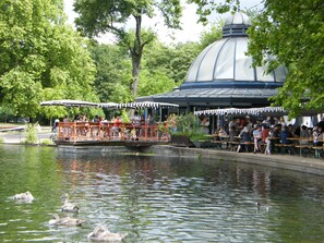 Un parque con un estanque, patos, un bote y un pabellón.