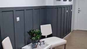 A hallway with a reception desk, two white cushioned seating areas, a potted plant, and framed pictures on the walls. - Optimus Comfort Fusta 9 (Valencia)