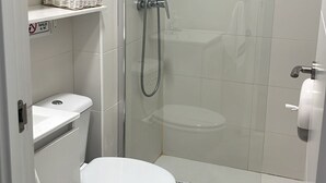 A small, modern bathroom with a toilet, shower, and a shelf with a basket. - Optimus Comfort Fusta 9 (Valencia)