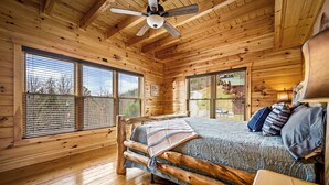 Ein Schlafzimmer in einer Blockhütte mit Bett, Holzwänden und großen Fenstern.