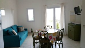 A small, bright room with a blue sofa, a round table with floral tablecloth, and a cabinet. - Mini-villa No. 9 - 2/4 people (PORTO VECCHIO)