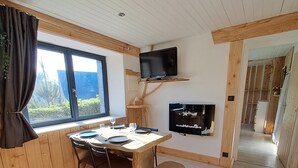 Une pièce chaleureuse avec une table à manger en bois, des chaises, un téléviseur fixé sur une étagère en bois et une fenêtre avec des rideaux.
