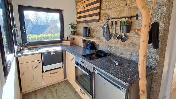 Une cuisine compacte avec des meubles en bois, un four encastré et un mur en pierre en arrière-plan.