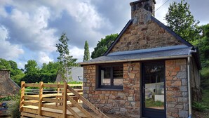 Une petite maison en pierre dotée d’une terrasse en bois et d’une rampe menant à l’entrée.