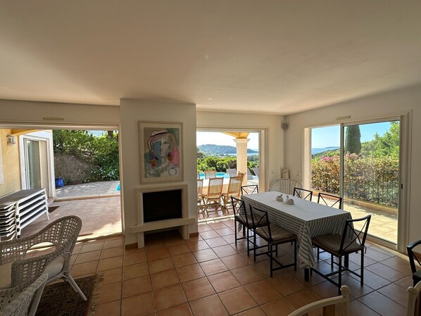 A spacious room with a dining area, a fireplace, and a large window offering a view of the outdoors. - Very quietly located 8-person villa with beautiful sea views and private pool. (Le Lavandou)