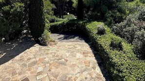 A stone pathway leading through a landscaped garden with various trees and shrubs, and a view of the sea in the distance. - Very quietly located 8-person villa with beautiful sea views and private pool. (Le Lavandou)
