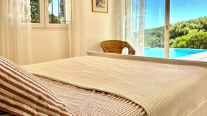 A bedroom with a large bed, a chair, and a view of a swimming pool and greenery. - Very quietly located 8-person villa with beautiful sea views and private pool. (Le Lavandou)
