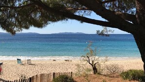 A beach with a wooden fence, a tree, and two blue chairs. - Very quietly located 8-person villa with beautiful sea views and private pool. (Le Lavandou)