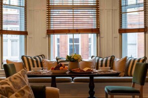 A dining area with a table set for two, featuring a bowl of fruit, a vase of flowers, and a plate of cheese.