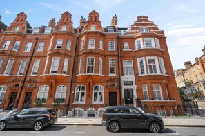 A row of red brick terraced houses with white window frames and a black car parked in front.