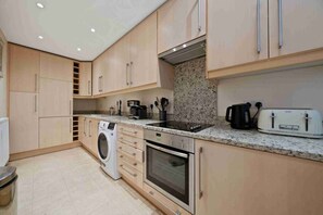 A modern kitchen with light wood cabinets, a built-in washing machine, a stainless steel oven, and a toaster.