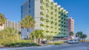 Een modern hotel met meerdere balkons, een parkeerplaats en palmbomen.