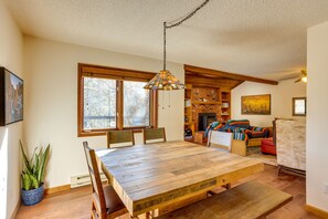 Un comedor amplio con una mesa y sillas de madera, una lámpara colgante y una chimenea de ladrillo al fondo.