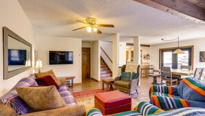 A spacious living room with a ceiling fan, a television, and a dining area with a staircase leading upstairs. - Near Trails! Sun-Drenched Durango Escape w/ View (Durango)