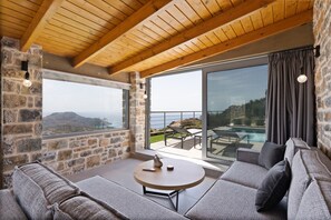 A cozy room with a stone wall, a wooden ceiling, a large window, and a balcony with a view.
