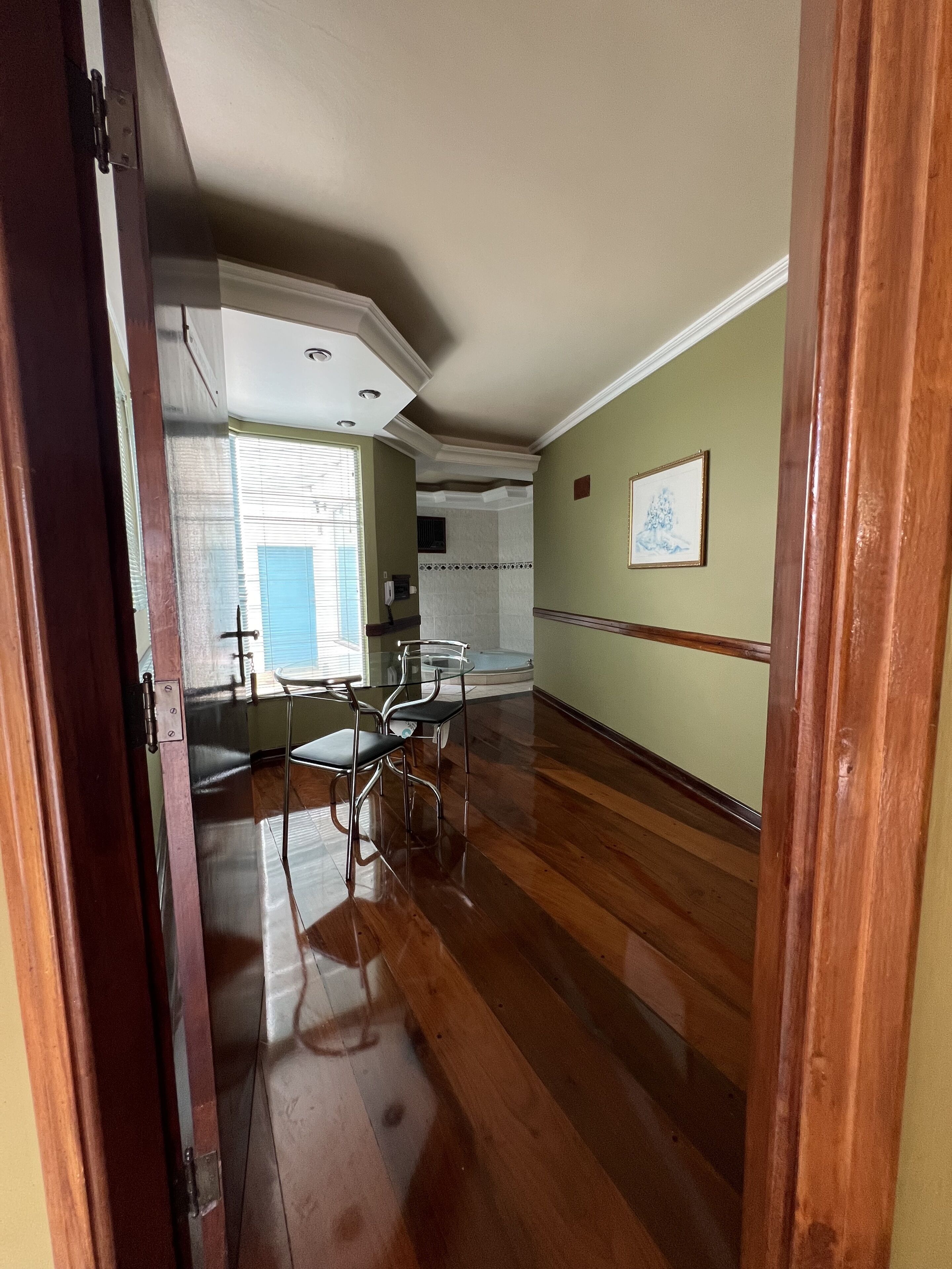 Um quarto espaçoso com piso de madeira, área de jantar com mesa e cadeiras, cozinha com pia e bancada, e um quadro na parede.