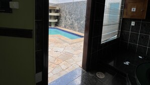 A bathroom with a large bathtub, a shower area, and a view of a swimming pool through a glass door. - Espacial Motel (Aracatuba)