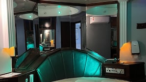 A modern hotel room with a curved ceiling, a large bed with two pillows, a nightstand with a lamp, and a mirror. - Espacial Motel (Aracatuba)