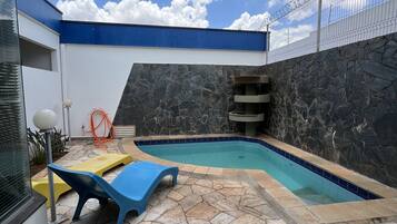 Piscina com ladrilhos de pedra e parede externa azul e branca.