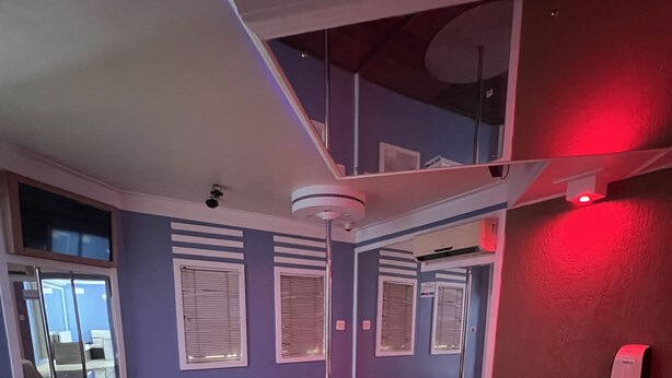 A modern bedroom with a curved bed, a ceiling fan, and a view of the outdoors through a large window. - Espacial Motel (Aracatuba)