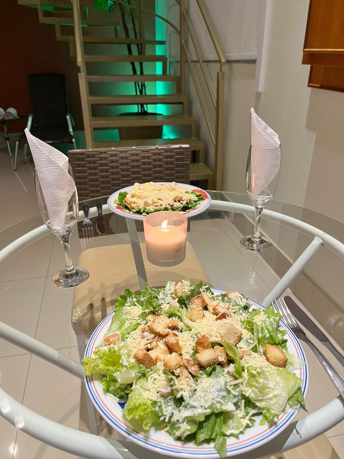 A dining table with a salad, two wine glasses, and a candle.