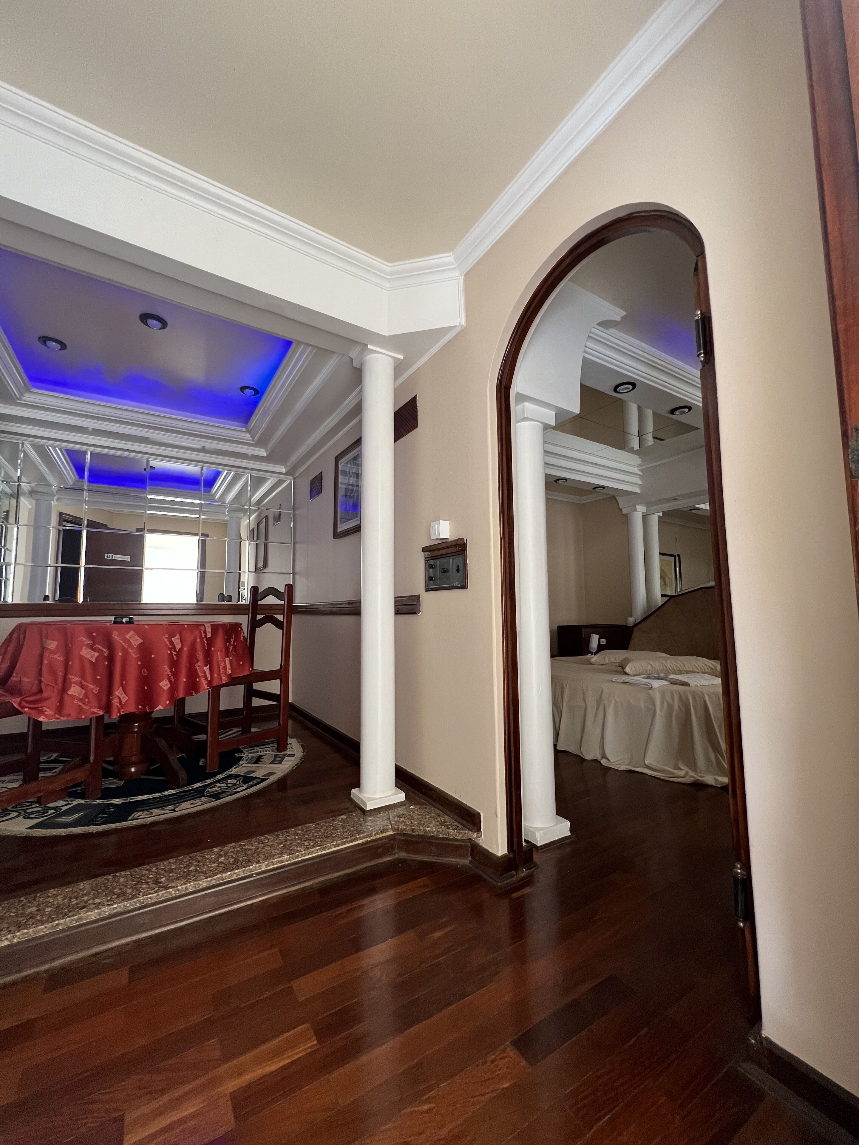 Habitación de hotel con piso de madera, un comedor con mantel rojo y un dormitorio con cama.