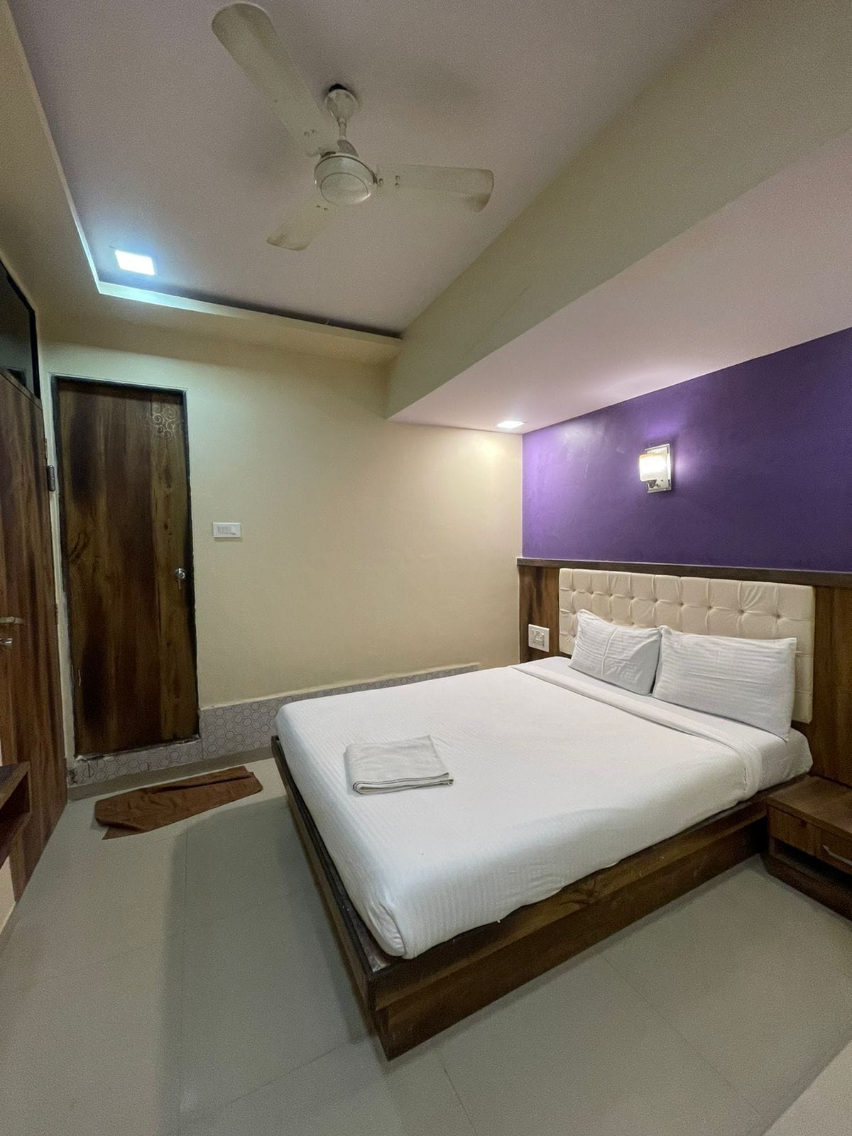 A bedroom with a bed, a ceiling fan, a wooden door, and a purple accent wall.