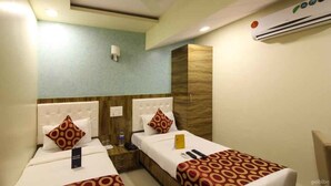 A hotel room with two beds, a wardrobe, a bedside table, and an air conditioning unit. - Hotel Western Court  (Mumbai)