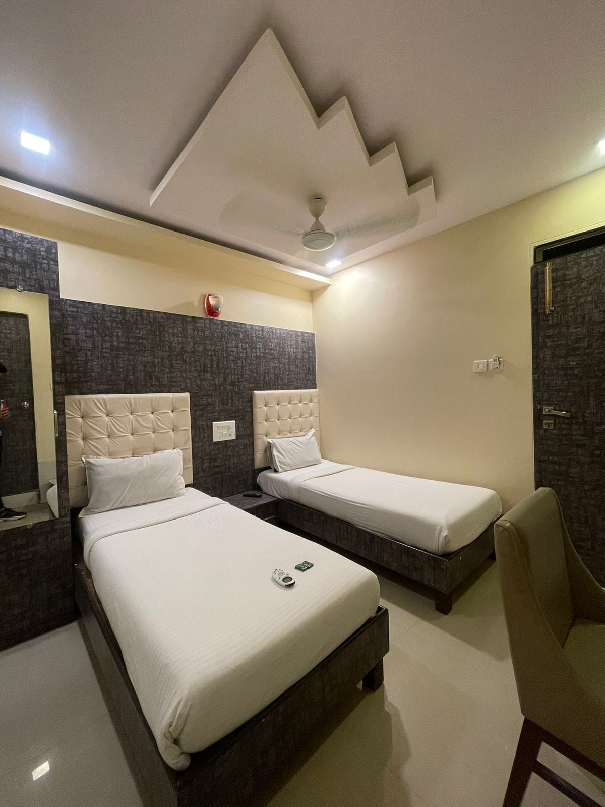 A hotel room with two beds, a mirror, a ceiling fan, and a door.