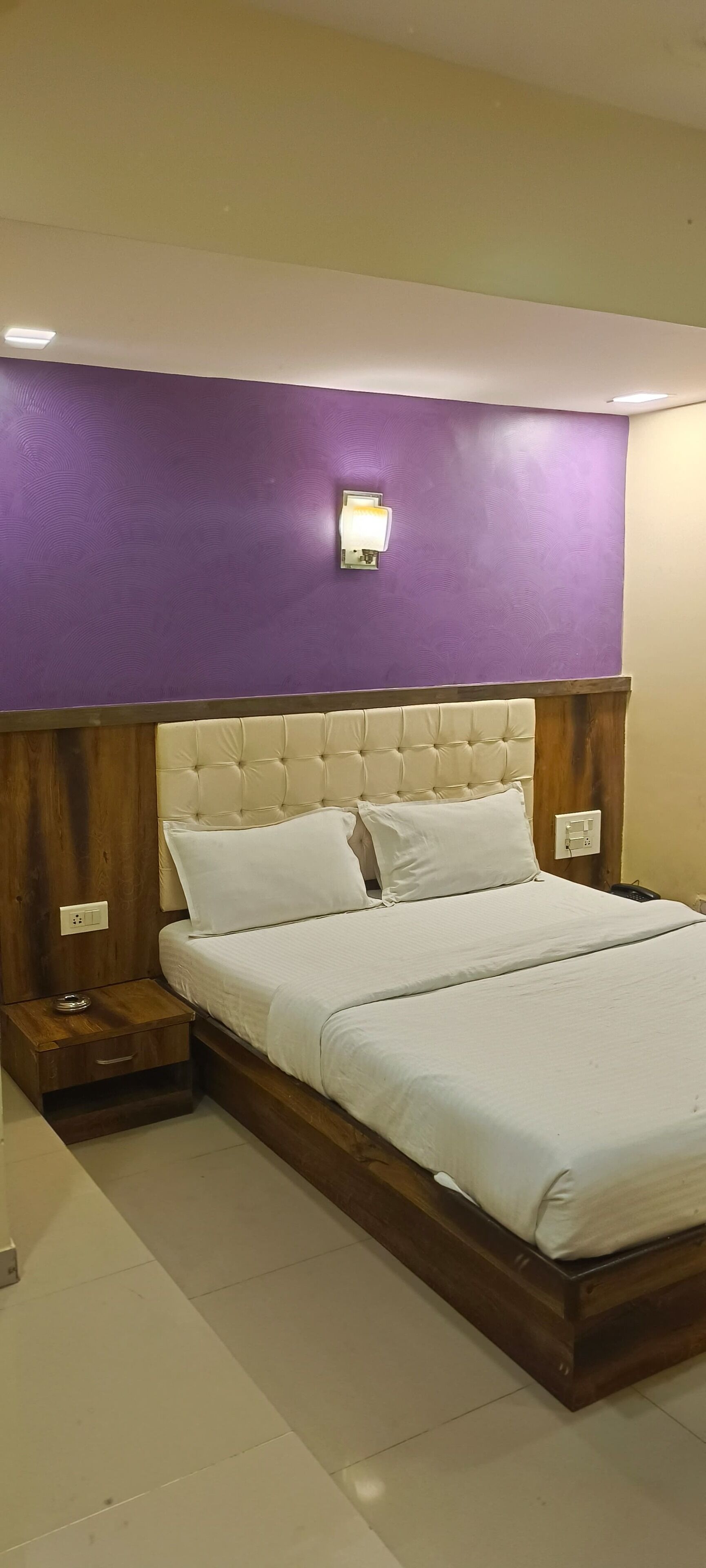 Une chambre avec un grand lit, une tête de lit en bois et un mur d’accent de couleur violette.