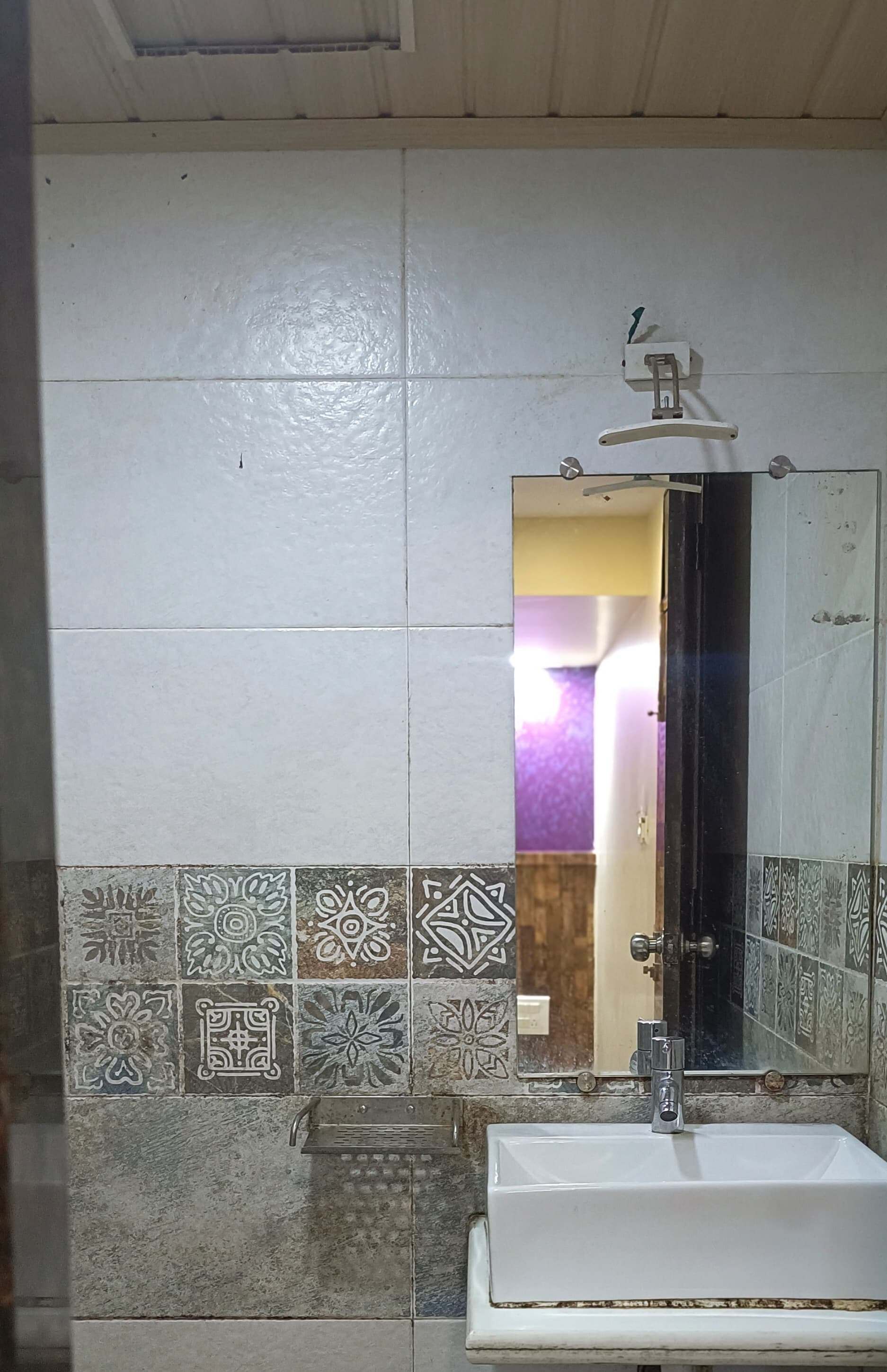 A bathroom with a white sink, a mirror, and patterned tiles on the walls.