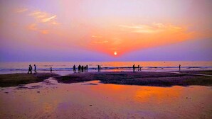 A beach with people walking along the shore during sunset. - Hotel Western Court  (Mumbai)