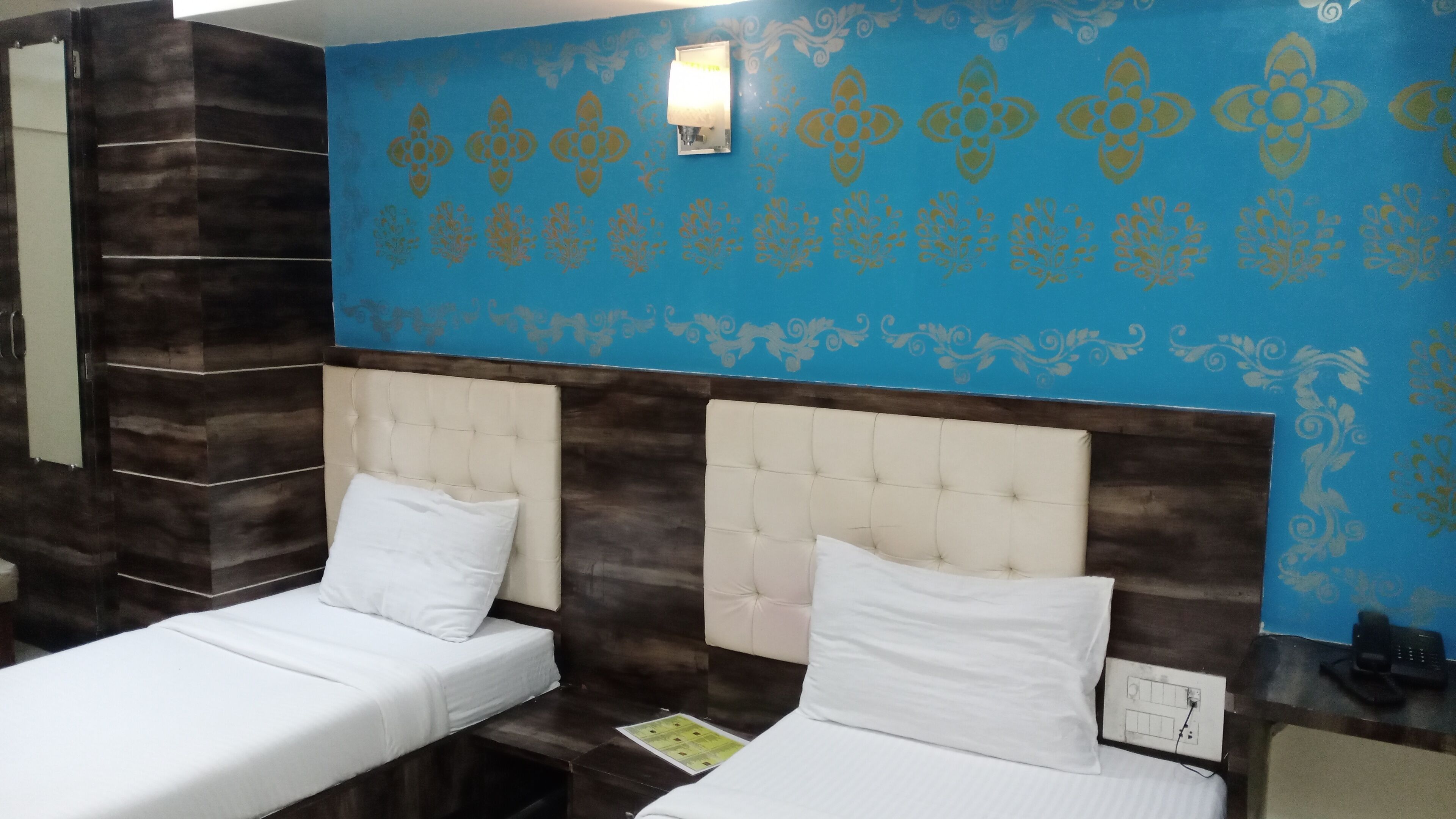 A hotel room with two beds, a blue patterned wall, and a wooden accent wall.