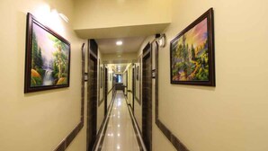 A hotel hallway with framed landscape paintings on the walls, a polished floor, and a ceiling light fixture. - Hotel Western Court  (Mumbai)