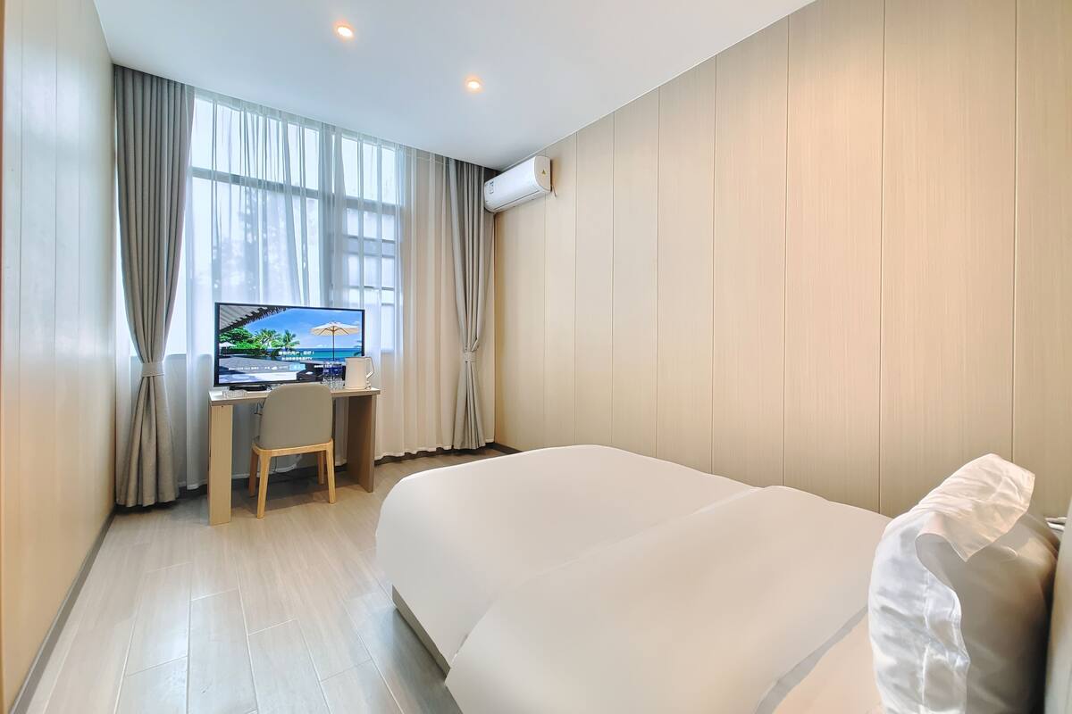 Ett hotellrum med en stor säng, ett skrivbord med en dator och en tv som visar ett tropiskt landskap.