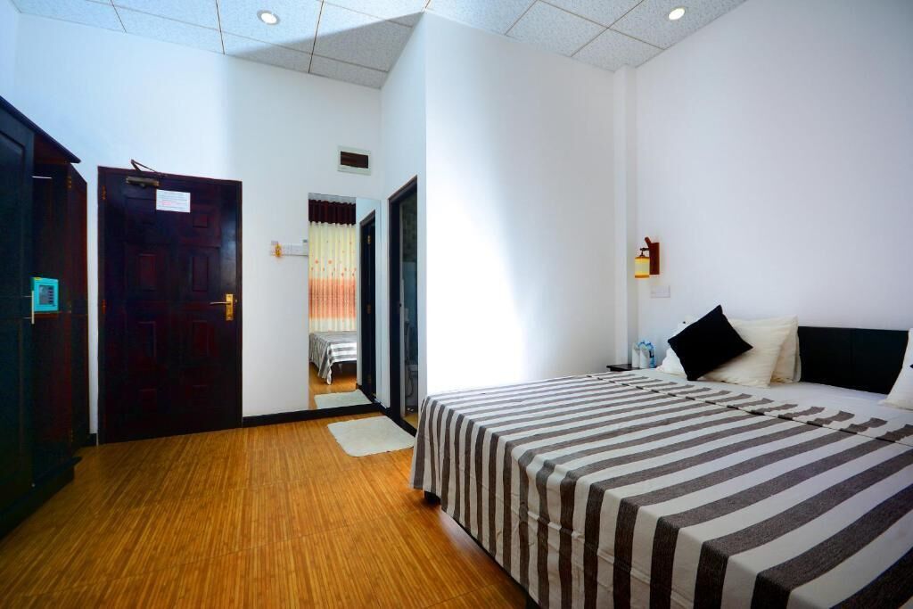 A hotel room with a large bed, wooden flooring, a door leading to a hallway, and a small window.