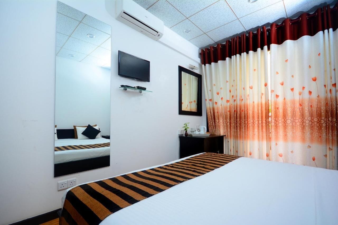 Une chambre d’hôtel avec un lit, une télévision, un miroir et une fenêtre avec des rideaux.
